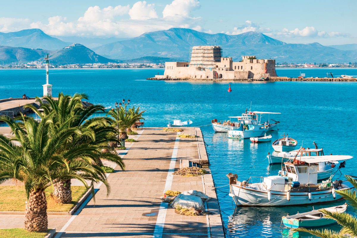 Beautiful port of Nafplio city in Greece with small boats, palm trees and Bourtzi castle on the water with selective focus